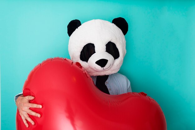 Hombre divertido en máscara de panda abrazando gran corazón rojo