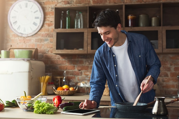 Hombre feliz cocinando comida sana con receta, mirando en tableta ...