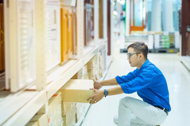 Hombre gerente asiático haciendo inventario de productos en caja de cartón en los estantes del almacén con tableta digital y pluma. asistente profesional masculino comprobación de stock en fábrica. recuento de inventario físico. Foto Premium