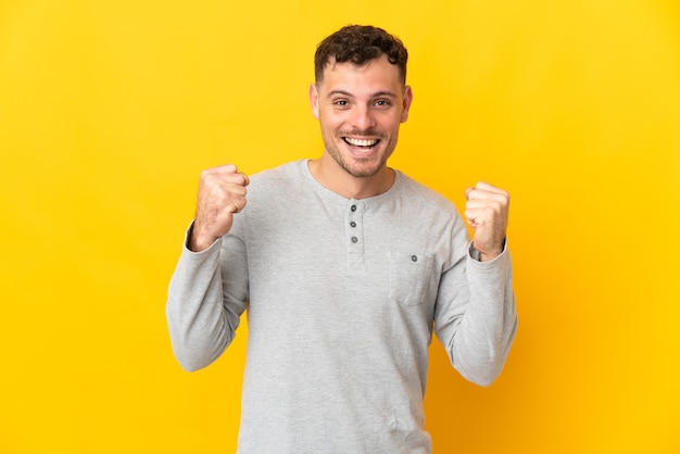 Hombre guapo caucásico joven aislado en la pared amarilla celebrando