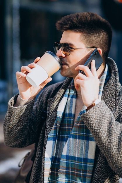 Hombre guapo joven tomando café fuera y usando el teléfono