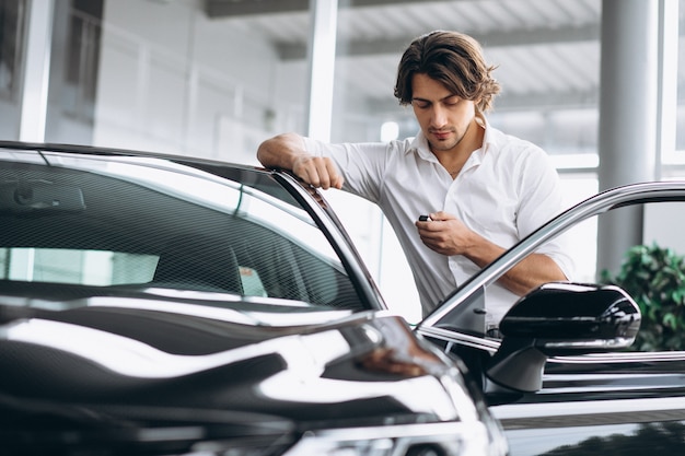 Hombre hermoso joven que sostiene llaves en una sala de exposición del coche Foto gratis