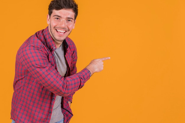Hombre joven feliz que señala su dedo en un fondo anaranjado Foto gratis