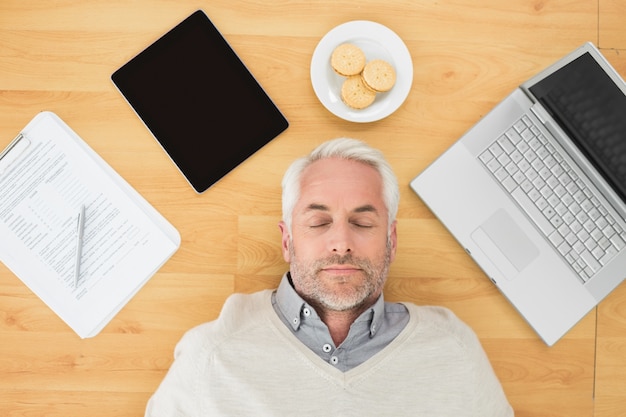 Hombre maduro durmiendo con electrónica y galletas en el piso de parquet Foto Premium