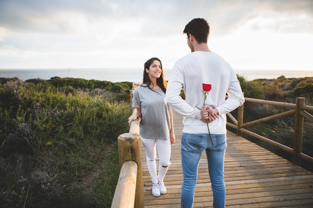 Hombre Mirando A Su Novia Mientras Esconde Una Rosa En Su Espalda Foto Gratis