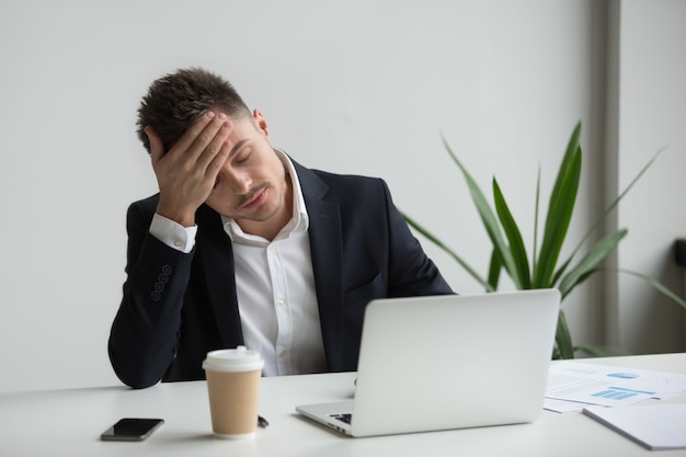 Hombre de negocios del milenio frustrado que tiene fuerte dolor de cabeza cansado de trabajo portÃ¡til Foto gratis