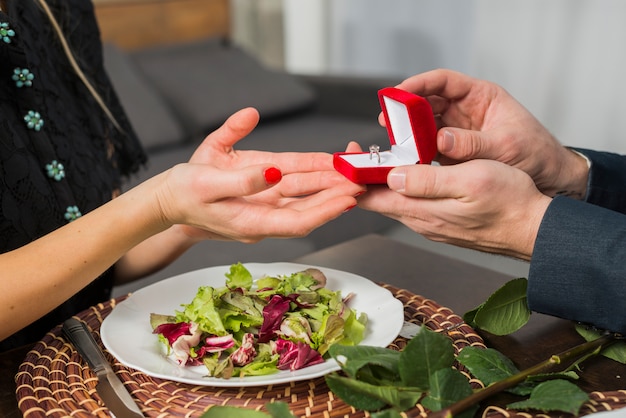 Hombre presentando caja de regalo con anillo a mujer en mesa con plato Foto gratis