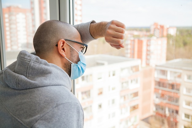 Hombre solitario en máscara médica mirando por la ventana | Foto Premium