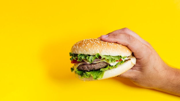 Hombre sujetando hamburguesa delante de fondo amarillo Foto gratis
