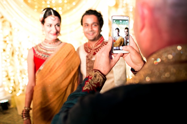 Hombre toma el cuadro de la boda hindú pareja en su teléfono inteligente Foto Gratis Hombre toma el cuadro de la boda hindú pareja en su teléfono inteligente Foto Gratis