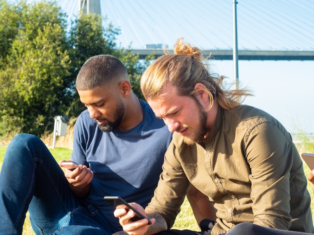 Hombres enfocados usando teléfonos inteligentes al aire libre Foto gratis