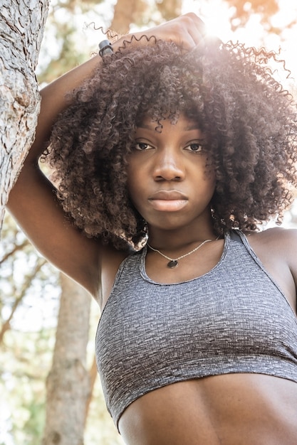 Imagen vertical de la joven chica de pelo afro apoyado en un árbol con