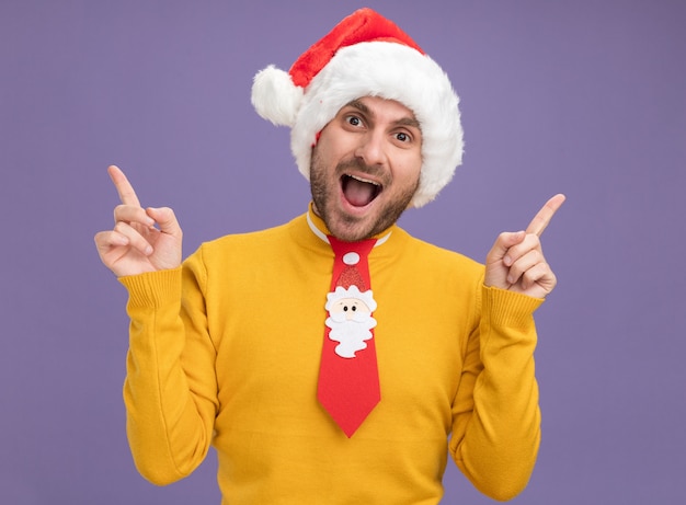 Impresionado joven caucásico vistiendo gorro de navidad y corbata