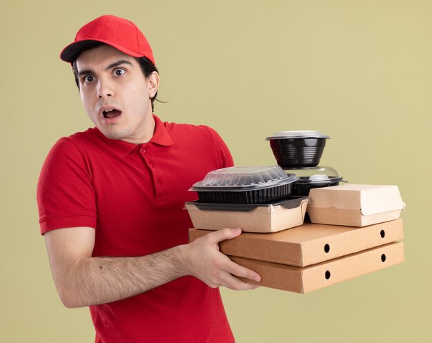 Impresionado Joven Repartidor Caucásico En Uniforme Rojo Y Gorra Sosteniendo Paquetes De Pizza 6652