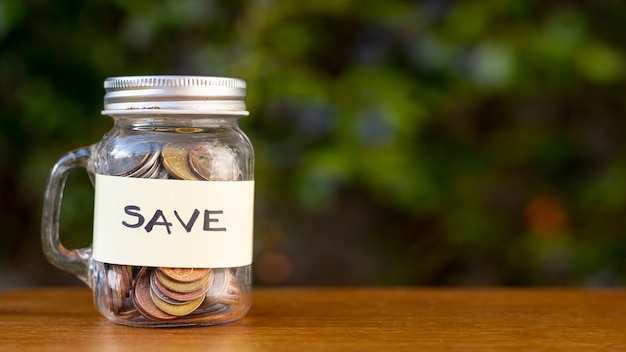 Jar con monedas y guardar la etiqueta al aire libre Foto gratis