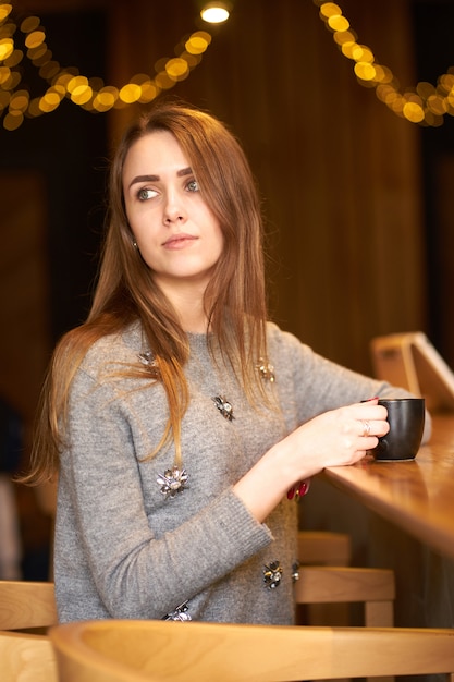 Joven Y Atractiva Mujer Pelirroja Atractiva Con Cabello Largo Y Maquillaje Natural Emplazamiento En El Cafe Y Sosteniendo La Taza De Cafe Negro Foto Premium