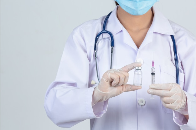 Joven médico sostiene una jeringa hipodérmica con guantes de goma vial vial en la pared gris. Foto gratis