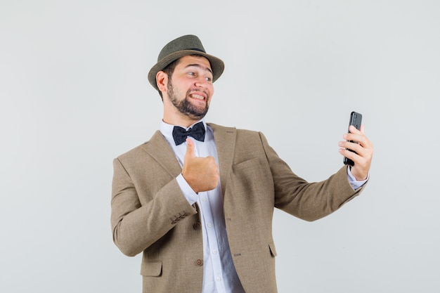 Joven Mostrando El Pulgar Hacia Arriba Mientras Toma Selfie En Traje Sombrero Y Mirando Alegre 