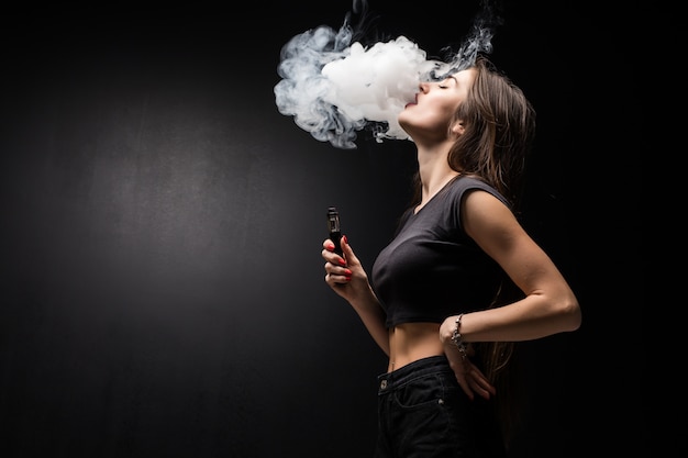 Joven mujer sexy vaping fumar cigarrillo electrónico nube de vapor en la pared negra Foto Gratis