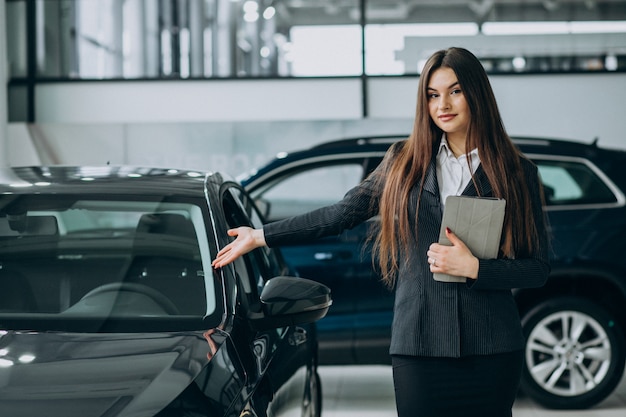 Joven mujer de ventas en carshowroom de pie junto al coche | Foto Gratis