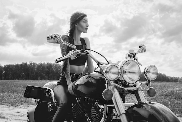 Jovencita sexy posando en una motocicleta al atardecer. concepto de