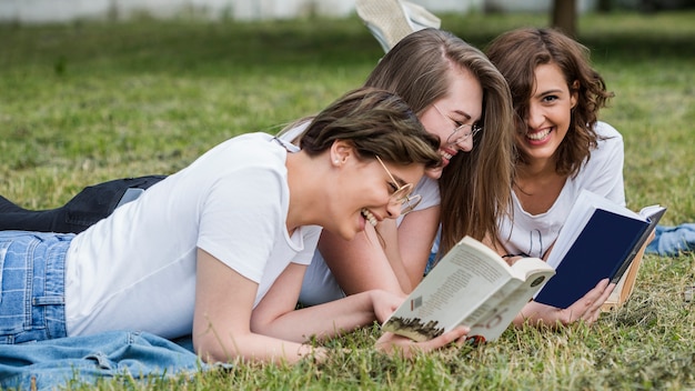 Jóvenes amigos leyendo tumbado en el césped del parque Foto gratis