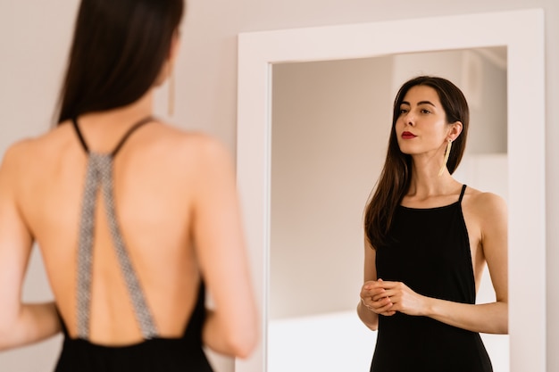 Lady lleva un hermoso vestido negro mirándose al espejo Foto gratis