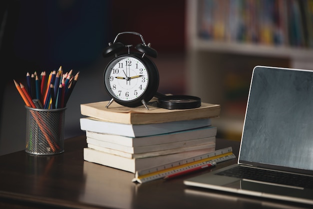 Libro, computadora portátil, lápiz, reloj en la mesa de madera en la biblioteca, concepto de aprendizaje educativo Foto gratis
