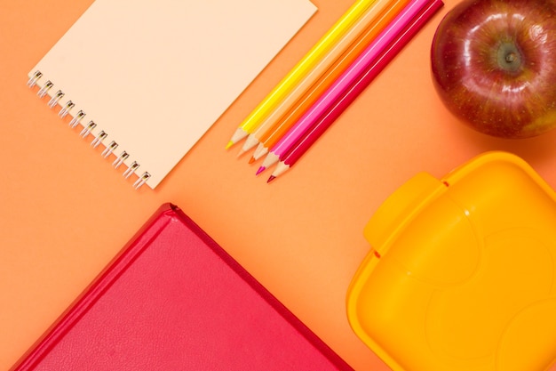 Libro cuaderno lápices de colores manzana roja y lonchera sobre