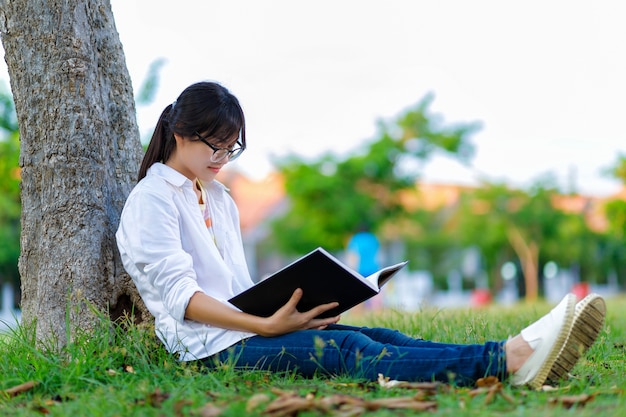 Libro de lectura asiático de la muchacha debajo del árbol en parque