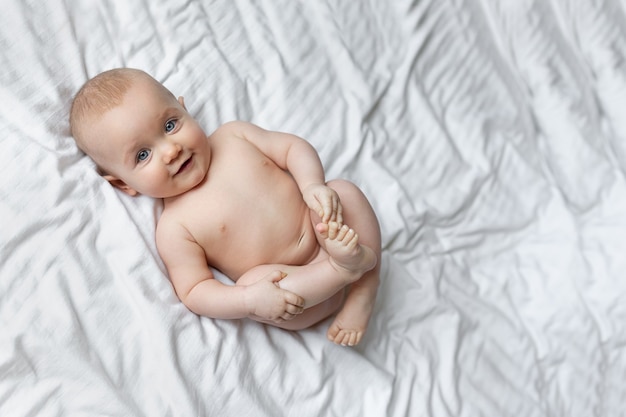 Un Lindo Bebe Esta Sonriendo Se Encuentra En Una Cama Enorme Con Sabanas Blancas Foto Premium