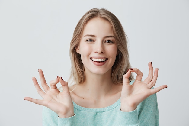 Lo estoy haciendo genial. me alegro feliz joven mujer rubia en suéter azul  sonriendo ampliamente y