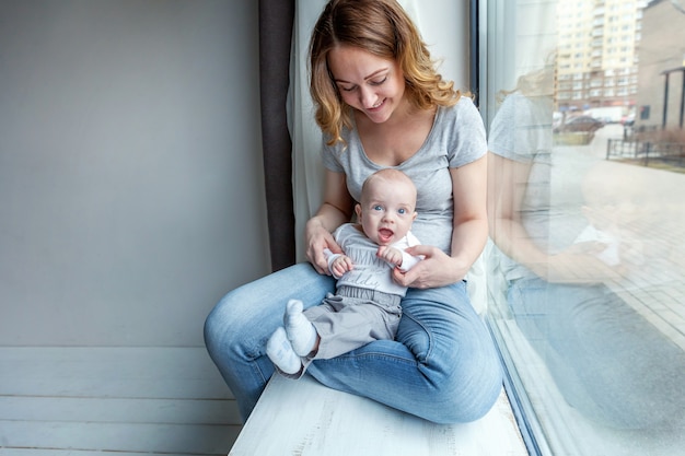 Madre joven que celebra al niño recién nacido. el niño de la mujer y del niño se relaja y jugando en dormitorio cerca de ventana Foto Premium
