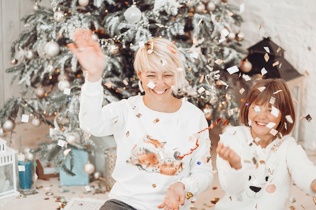 Mamá e hija se divierten jugando antes de un árbol de navidad Foto