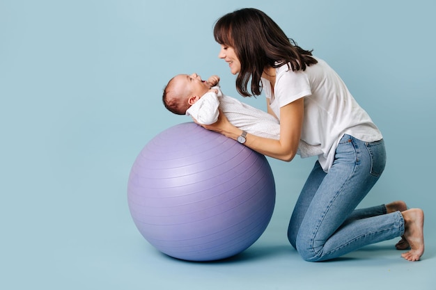 Mamá Morena Hermosa Joven Hace Ejercicios Con El Bebé En La Pelota De Fitness El Bebé Se Ríe 9098