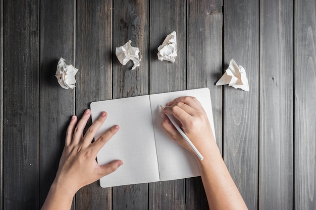 Mano escribiendo junto a algunas bolas de papel