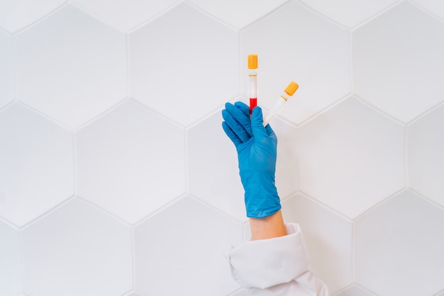 Una mano con guantes de goma sostiene dos tubos con el medicamento. Foto gratis