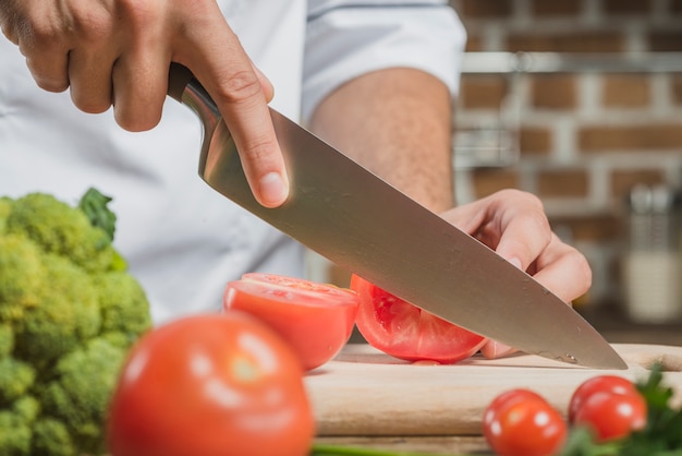 Mano Masculina Del Chef Cortar El Tomate Con Un Cuchillo Filoso A Bordo Foto Gratis