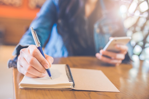 La mano de la mujer está escribiendo en libreta espiral vacía con ...