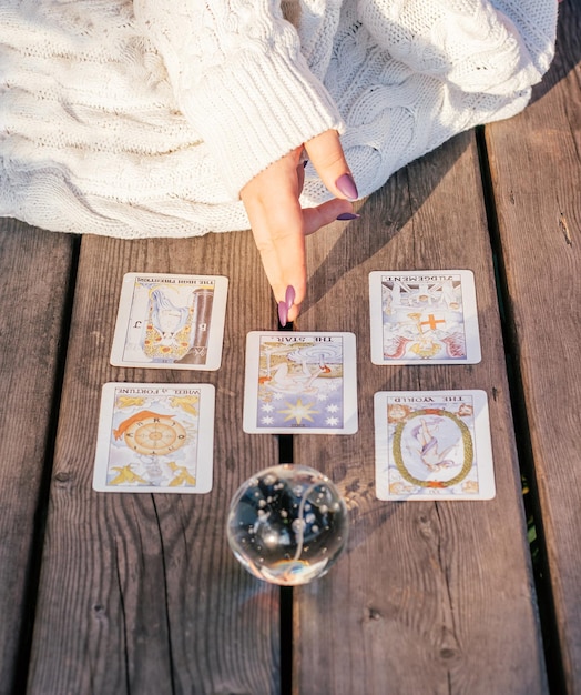 La mano de la mujer con uñas moradas apunta a cinco cartas del tarot esparcidas sobre una