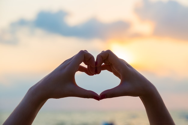 Las manos hacen en forma de corazón amor con silueta en el fondo del