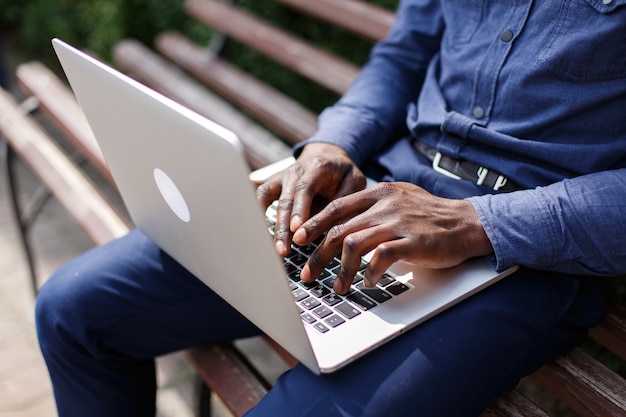 Manos del hombre afroamericano escribiendo algo en la computadora portÃ¡til mientras Ã©l se sienta en el banquillo