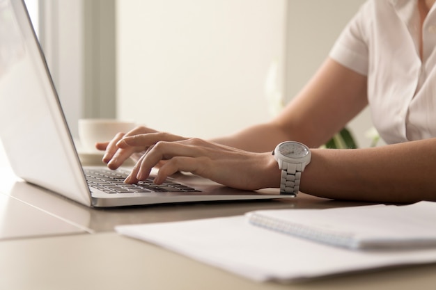 Las manos de la mujer que mecanografÃ­an en el ordenador portÃ¡til en el lugar de trabajo