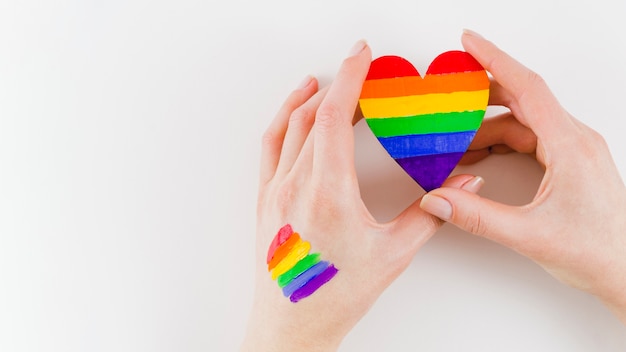 Manos sujetando un corazón con los colores de la bandera del orgullo Foto gratis