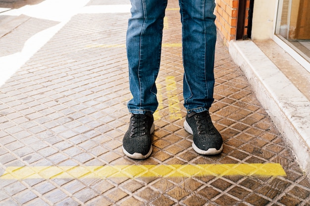 Mantenga la distancia social en la línea de espera amarilla adjunta en el  suelo. prespectiva de los pies de una persona. | Foto Premium