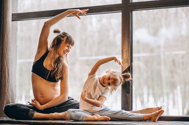 Mopther embarazada haciendo yoga con su pequeña hija Foto gratis