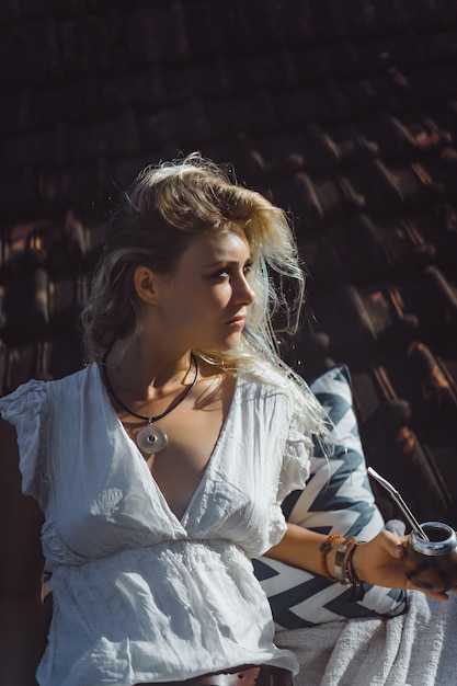Muchacha india hermosa del hippie con el pelo rubio largo en el té de consumición del compañero del tejado. Foto gratis