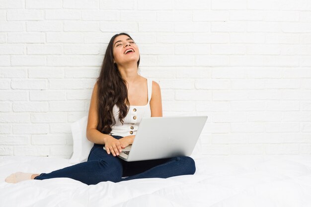 La mujer árabe joven que trabajaba con su computadora portátil en la cama rió relajado y feliz, el cuello estiró mostrando los dientes. | Foto Premium