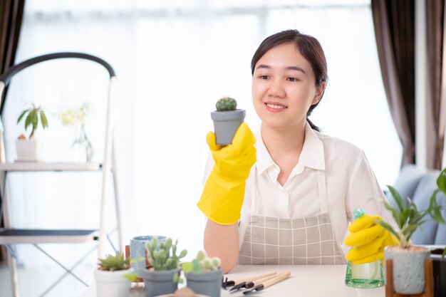 mujer asiática feliz alegre que riega una pequeña planta de interior en