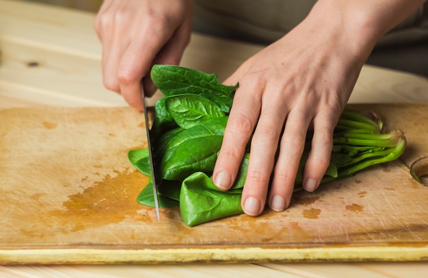 Una Mujer Está Cortando Espinacas En Un Tablero De Cocina. | Foto Premium